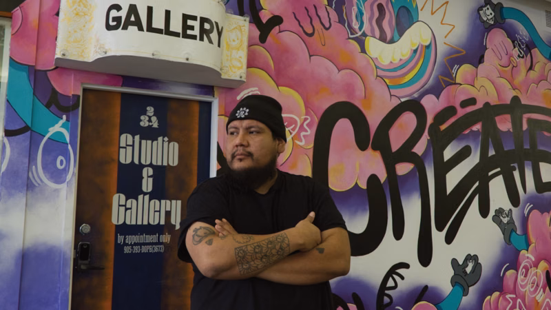 Dope Chief standing infront of his studio space, with a colorful mural behind him.